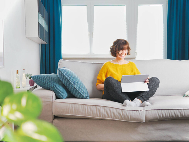 Mosolygó lány ülni pihenjen a kanapén a modern laptop.boldog fiatal nő szabadúszó munka a számítógépen otthonról. társadalmi-távolságtartó és elszigeteltségi koncepció. coronavirus maradjon otthon és online élő. - Fotó, kép