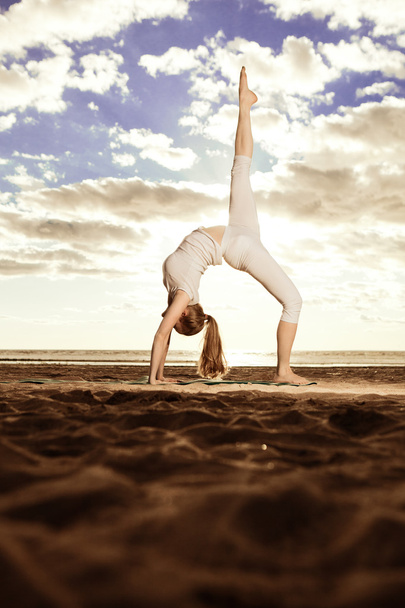 Young beautiful slim woman practices yoga on the beach at sunset - Fotoğraf, Görsel
