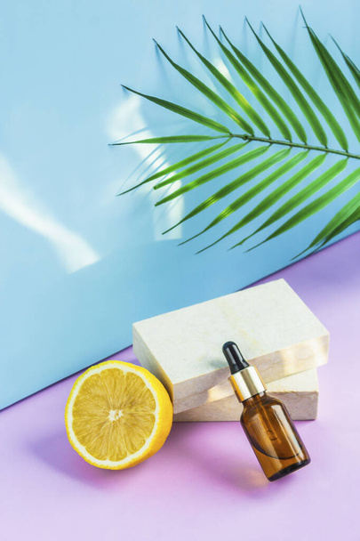 A cosmetic jar with an eyedropper stands on two granite slabs, like on a catwalk, next to half a yellow lemon, a palm leaf and the glare of the sun in the background. Cosmetics for summer. - Foto, Imagem