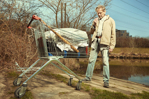 Older beggar man with his property in shopping cart - Zdjęcie, obraz