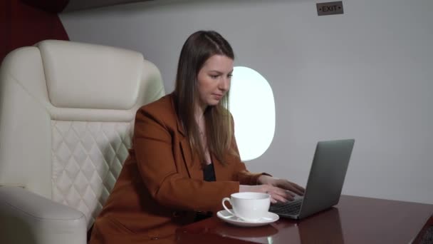 Woman in airplane working at laptop and drinking coffee. Businesswoman in private jet or first business class with computer. Luxury travel journey - Imágenes, Vídeo