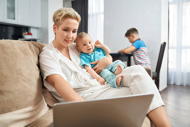 Pleasant woman working on laptop and carrying toddler - Photo, image