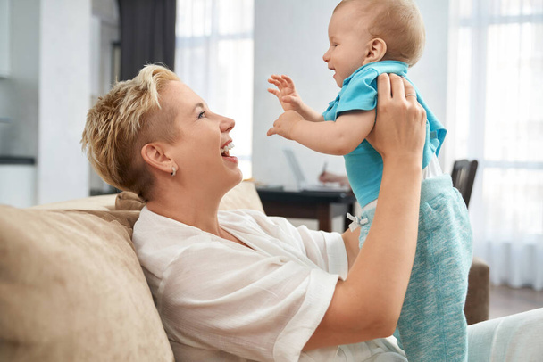 Cheerful woman playing with her little son on couch - Fotoğraf, Görsel