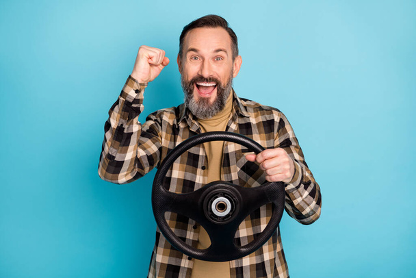 Photo portrait of man riding car keeping steering wheel gesturing like winner laughing isolated on vibrant blue color background - 写真・画像