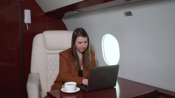 Woman in airplane working at laptop and drinking coffee. Businesswoman in private jet or first business class with computer. Luxury travel journey - Filmati, video