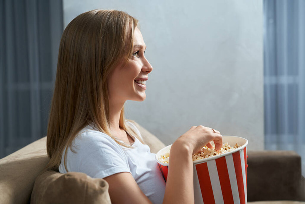 Beautiful blonde watching TV and eating popcorn - Foto, afbeelding