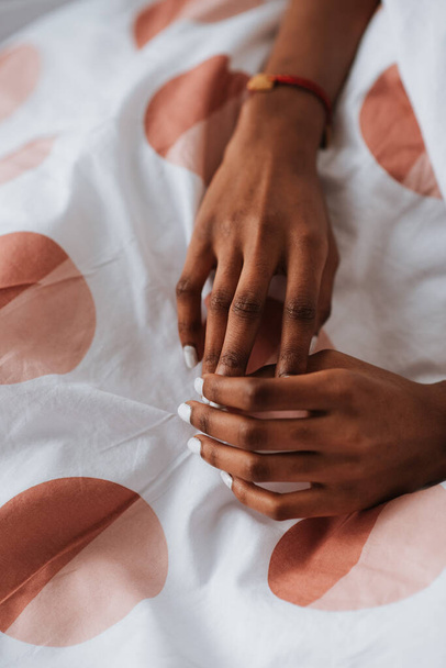 Young African female hands with white manicure on a bed - Fotó, kép