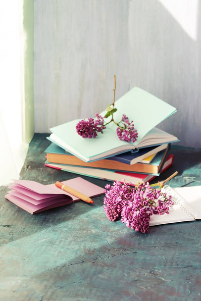 Bücher, Notizblöcke und frische Fliederblumen auf dem Tisch am Fenster, Schulkonzept zu Hause, zurück zur Schule - Foto, Bild