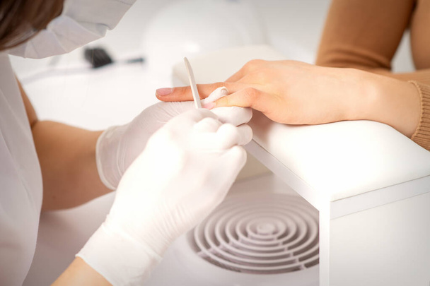 Gros plan de la main de la jeune femme recevant la procédure de lime à ongles dans un salon de beauté - Photo, image