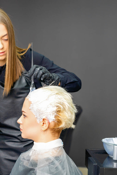 Femme coiffeurs teinture cheveux de jeune femme caucasienne dans le salon de coiffure - Photo, image
