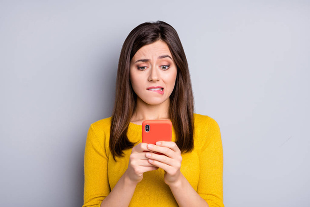 Photo of young unhappy upset sad girl bite lips using smartphone wear yellow pullover isolated on grey color background - Fotoğraf, Görsel