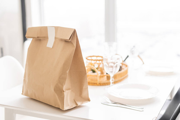 Obraz tła torby papierowej rzemieślniczej na drewnianym stole w białej kuchni wnętrza z etykietą żywności ekologicznej, usługi dostarczania żywności, przestrzeń do kopiowania. - Zdjęcie, obraz