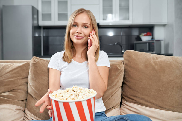 Attractive woman talking on mobile and eating popcorn - Foto, afbeelding