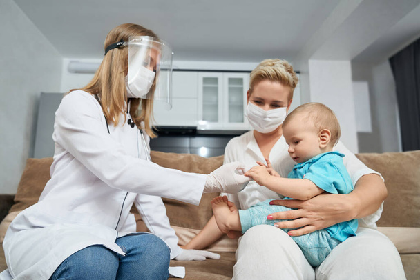 Female doctor in mask examining baby at home - Foto, afbeelding