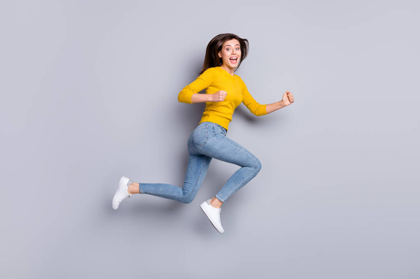 Full size profile photo of hooray brunette nice lady jump run wear yellow sweater jeans sneakers isolated on grey color background - Fotografie, Obrázek