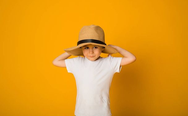 portrait of a little boy in a white T-shirt and straw hat on a yellow background with space for text - Foto, Imagem