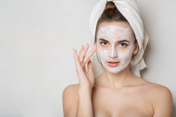 Piękna młoda kobieta z ręcznikiem kąpielowym na głowie przy użyciu maski nawilżającej na twarzy. Osobista opieka w domu. Miejsce na tekst - Zdjęcie, obraz