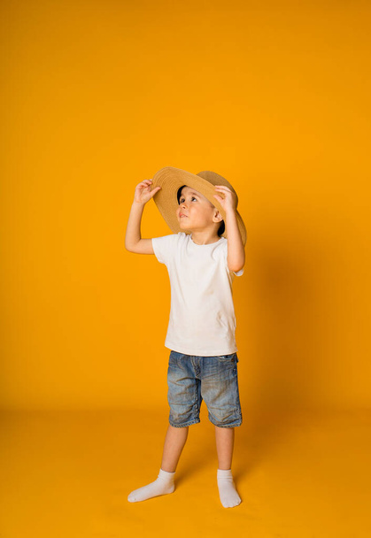 Hasır şapkalı küçük bir çocuk sarı arka planda duruyor ve mesaj için yeri var. - Fotoğraf, Görsel