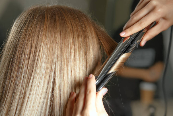 O cabeleireiro faz argolinhas com ferro a uma jovem loira no salão de beleza. Tiro de perto - Foto, Imagem