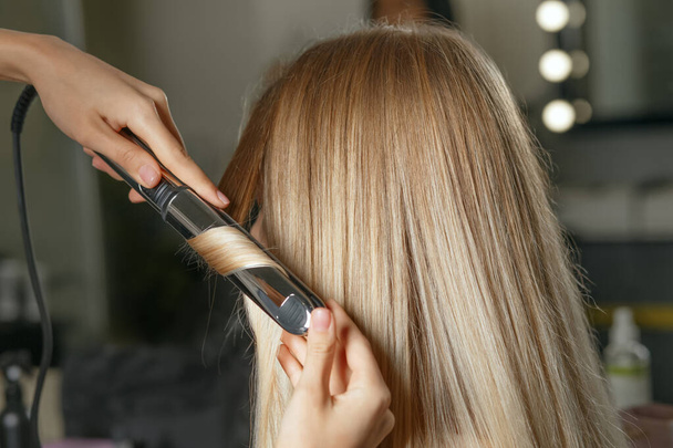 Friseur macht einem Kunden im Schönheitssalon Klingelbeutel mit Lockenstab. Nahaufnahme - Foto, Bild