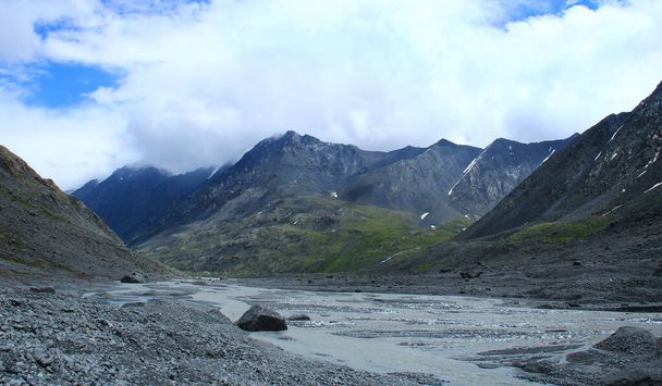 Rzeka płynąca z lodowca Sofii w górskim wąwozie w Altai, skaliste zbocza i szczyty grzbietów, kamienne brzegi rzek, gęste chmury, lato, słoneczny - Zdjęcie, obraz