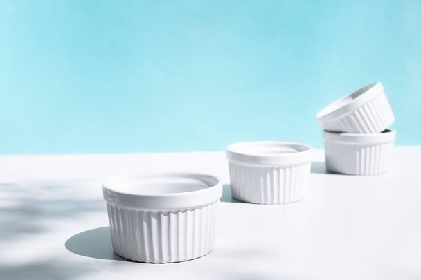 Stack of four white ceramic bowls on blue pastel background with hard shadows. Creative kitchen tableware. - 写真・画像