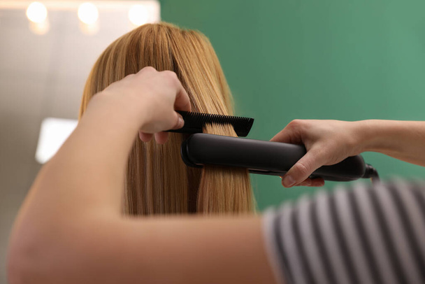 Stylist straightening woman's hair with flat iron in salon - Фото, изображение