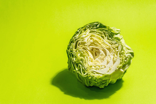 Fresh young cabbage, half a head in bright green background. Modern hard light, dark shadow.Vegetables for cutting spring salad. Vegan food, diet, vitamins - Photo, Image