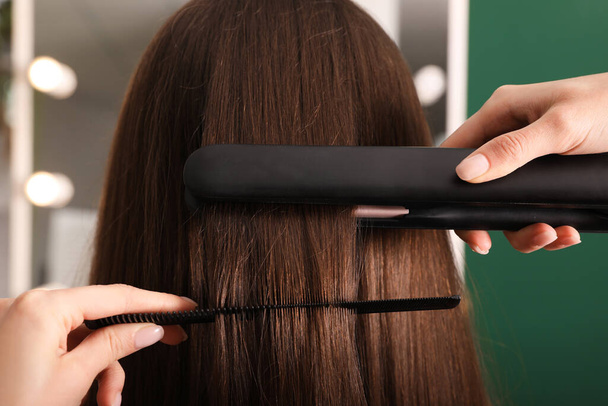 Stylist straightening woman's hair with flat iron in salon - Foto, imagen