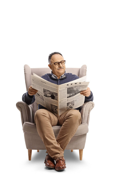 Mature man reading a newspaper seated in an armchair isolated on white background - Foto, Imagem