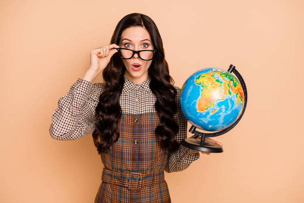 Portrait of lovely amazed wavy-haired teacher holding in hands globe explore world pout lips isolated on beige pastel color background - Foto, Imagem
