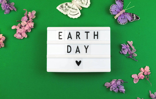 Earth Day felirat egy villanydoboz, lapos laikus és kreatív háttér virágokkal és tavaszi pillangó, felülnézet - Fotó, kép