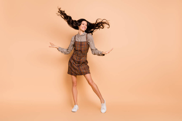 Full length body size view of attractive cheery wavy-haired girl wearing checked uniform dancing isolated on beige pastel color background - Zdjęcie, obraz