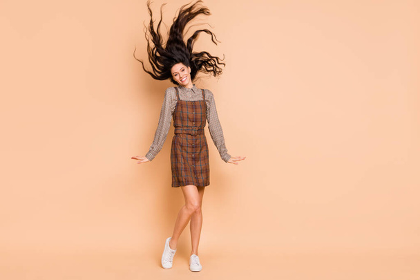 Full length body size view of pretty cheery girl wearing checked uniform having fun throwing wavy hair isolated on beige pastel color background - Photo, image