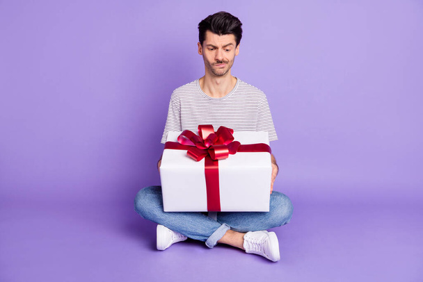 Photo of suspicious guy hold giftbox grimace wear striped white t-shirt jeans footwear isolated violet background - Fotografie, Obrázek