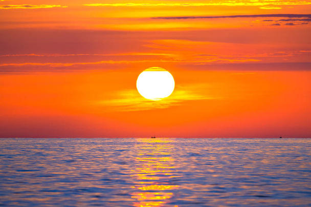Sun rising in the sea with a fishing boat in the rays of the sun above the waves. Beautiful sunrise on the ocean with a big and colorful sun in summer. A new day begins. - Photo, Image
