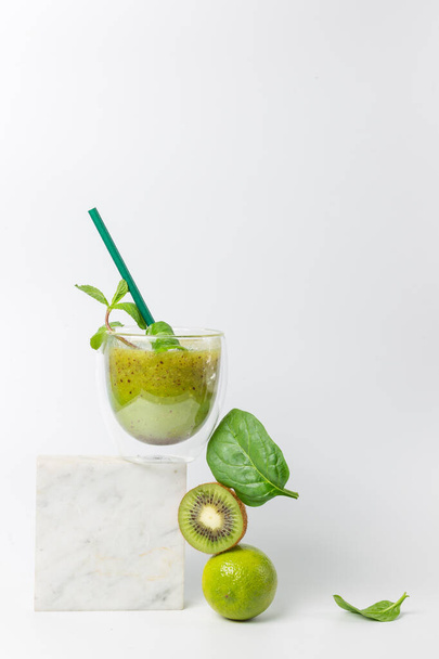 Still life concept of a balanced diet. Detox smoothie with kiwi, lime, spinach and mint. On a marble stand over a white background. Balancing food, refreshing cocktail. Vertical - Photo, image