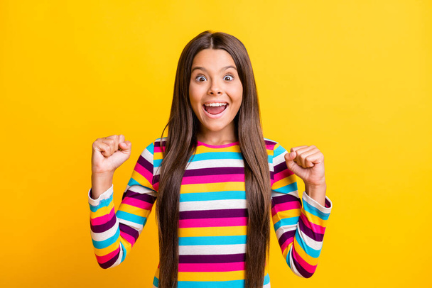 Photo of small girl open mouth raise fists amazed look camera wear striped shirt isolated yellow color background - Foto, Bild