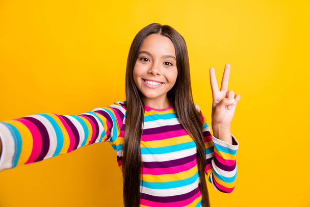 Photo of little adorable girl take selfie show v-sign beaming smile wear striped shirt isolated yellow color background - Foto, afbeelding