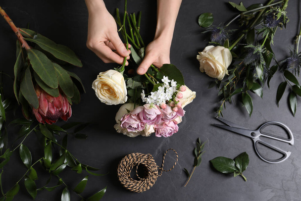 Florist making beautiful bouquet at black table, top view - Fotó, kép