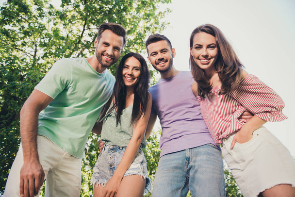 Low angle view photo of four attractive men and woman hug each other friends beaming happy smile rest in park outside in outdoors - Фото, изображение