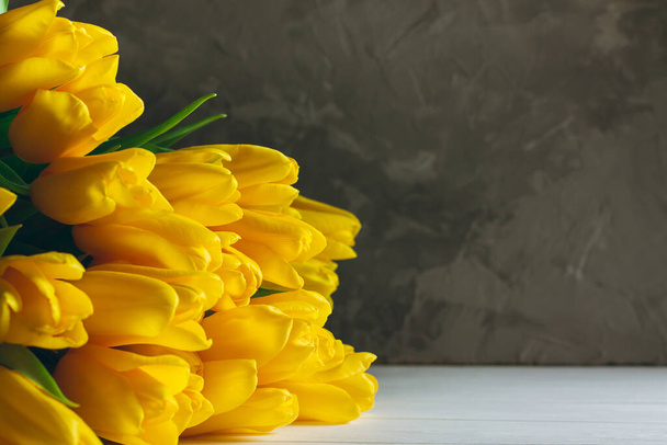 Bouquet of bright yellow tulips lying on white wooden surface on gray background, copy space - Fotografie, Obrázek