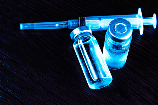 2 doses Sars-Kov-2 coronavirus vaccin in transparante glazen ampullen, bedekt met vorst en een wegwerpspuit, op een donkere achtergrond, korte focus, toning  - Foto, afbeelding