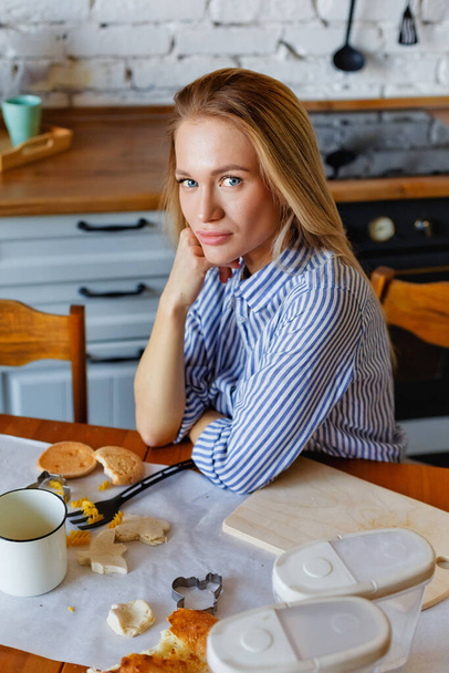 Mladá krásná blondýnka v modré pruhované košili sedí u stolu. - Fotografie, Obrázek