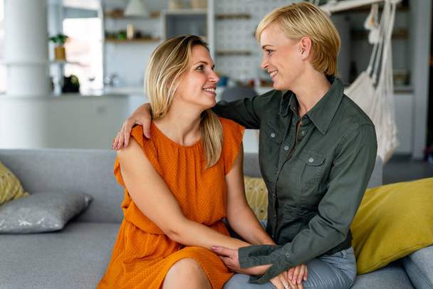 Portrait of happy young lesbian couple embracing each other and smiling in living room - Foto, Imagen