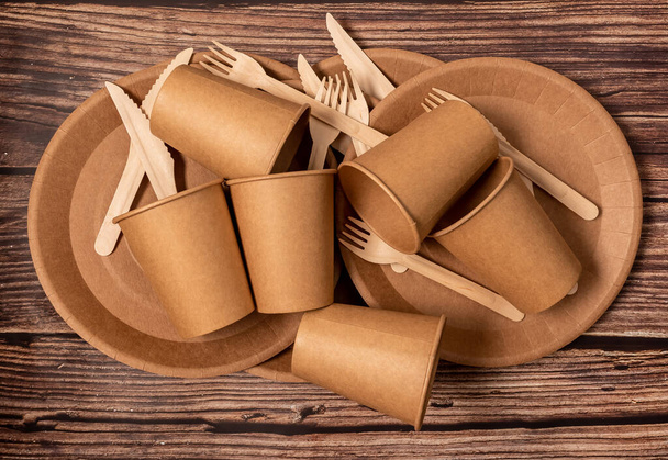 The craft package contains disposable tableware, forks, knives and glasses. On a wooden brown background. - Foto, Imagen