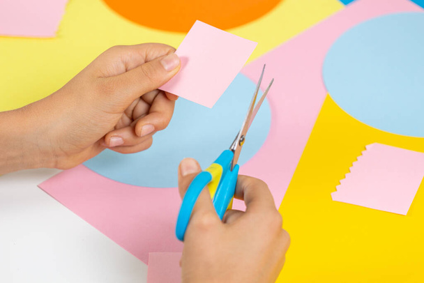 Mains coupant du papier coloré avec des ciseaux. Éducation, apprentissage, artisanat du papier, divertissement à la maison - Photo, image