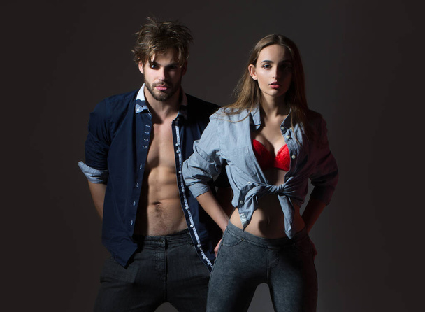 Young sexy couple of pretty girl or beautiful woman in red sexy bra and handsome man muscular macho in unbutton shirts on grey wall. - Fotó, kép