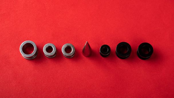 пирсинг, украшения для ушей, ушные туннели в черном и серебристом цветах с расширителем в ряд на красном фоне - Фото, изображение