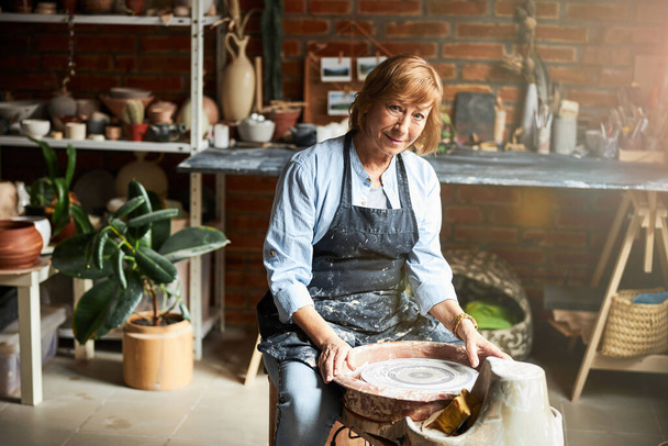 Charming old woman working in pottery workshop - Photo, Image